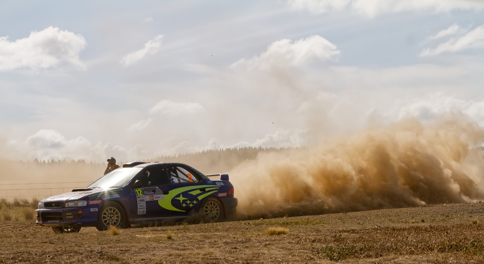Rally car with photographer seeming to be dangling out of the driver's window...